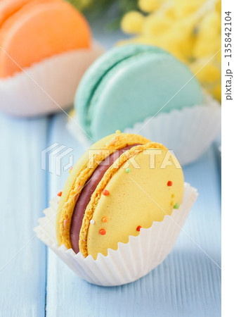 Colorful French macarons in paper liners on a blue wooden surface with mimosa flowers, spring concept 135842104