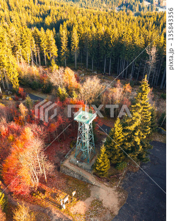 Slovanka Lookout Tower stands tall in the Jizera Mountains, surrounded by vibrant autumn foliage. The oldest iron tower in the Czech Republic offers stunning views of the forest. 135843356