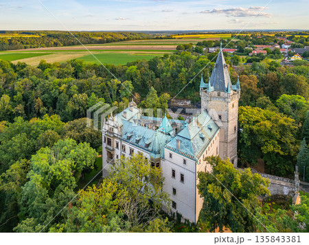 Stranov Castle overlooks lush greenery in Central Bohemia. This aerial view captures its stunning architecture surrounded by vibrant trees and fields, showcasing the region's beauty. 135843381