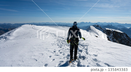 A climber makes their way to the summit of Piz Palu, surrounded by stunning glaciers and majestic alpine views. The bright summer sun shines over the snow-covered ridge. A climber makes their way to the summit of Piz Palu, surrounded by stunning glaciers and majestic alpine views. The bright summer sun shines over the snow-covered ridge. 135843383