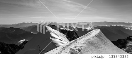 Hikers navigate the exposed summit ridge of Piz Palu, enjoying breathtaking views of the surrounding peaks in summer. Snow covers the sharp, steep path above the glacier. 135843385