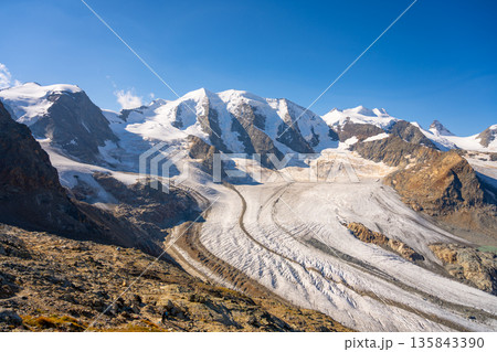 Piz Palu stands tall among rocky ridges, showcasing the vast Pers Glacier. Sunlight highlights the snowy peaks, creating a stunning alpine landscape in Switzerland’s high mountains. Piz Palu stands tall among rocky ridges, showcasing the vast Pers Glacier. Sunlight highlights the snowy peaks, creating a stunning alpine landscape in Switzerland’s high mountains. 135843390