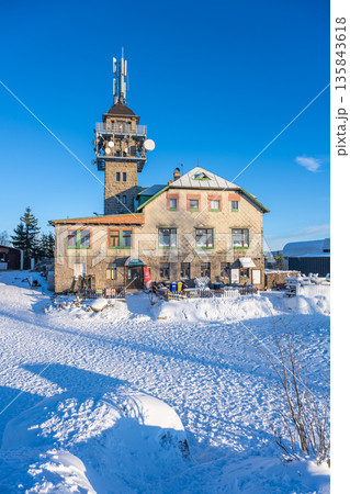 The lookout tower at Tanvaldsky Spicak stands in winter. Snow covers the ground around the structure. Visitors explore and enjoy the mountains in the Jizera region. The lookout tower at Tanvaldsky Spicak stands in winter. Snow covers the ground around the structure. Visitors explore and enjoy the mountains in the Jizera region. 135843618