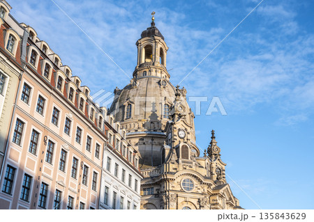 Frauenkirche in Dresden showcases its large dome against a blue sky. The church is surrounded by historic buildings, creating an interesting view. Many visitors enjoy the scenery. 135843629