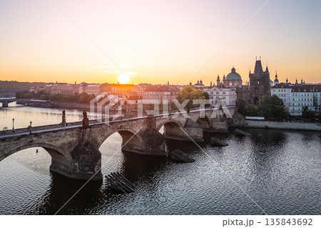 Golden sunlight illuminates Charles Bridge in Prague at dawn. The iconic structure stands gracefully over the Vltava River, creating a stunning urban panorama without crowds. 135843692