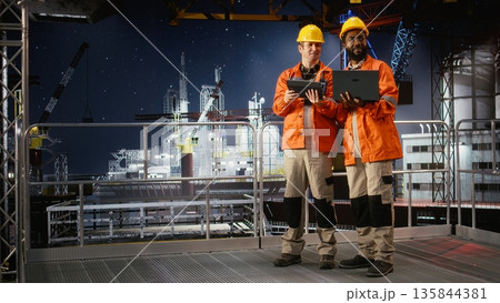 Portrait of engineers work on offshore oil rig platform late at night, analyzing drilling operations with gadgets to ensure efficient fuels and gasoline extraction for oil industry. 135844381