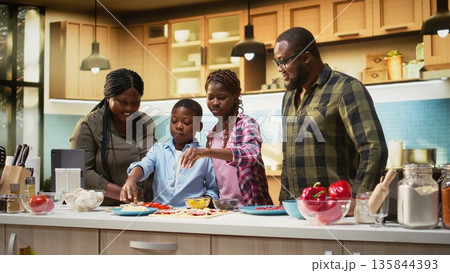 Smiling children help parents prepare pizza by sprinkling grated cheese in the kitchen, family cooking activity during the weekend. Cozy moment of teamwork and meal preparation. Camera A. Smiling children help parents prepare pizza by sprinkling grated cheese in the kitchen, family cooking activity during the weekend. Cozy moment of teamwork and meal preparation. Camera A. 135844393