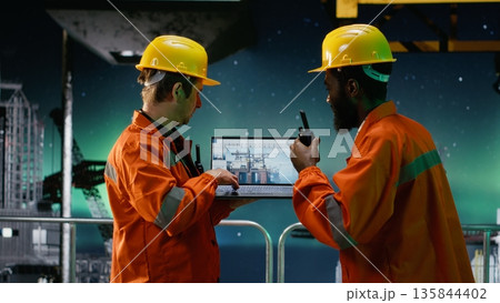 Offshore engineers communicate via walkie talkie at night on oil platform under the aurora borealis, ensuring oil and gas emission tracking and safe drilling rig operations. 135844402