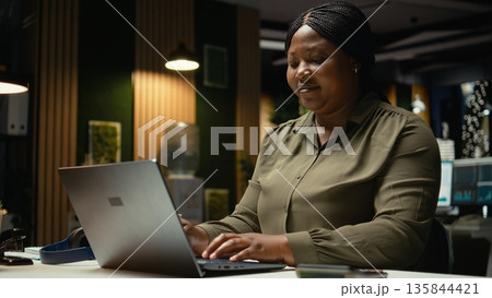 Black businesswoman typing data reports and managing information on laptop, drafting reports and proofreading to solve tasks. Notetaking supports goal setting for the enterprise. Camera A. Black businesswoman typing data reports and managing information on laptop, drafting reports and proofreading to solve tasks. Notetaking supports goal setting for the enterprise. Camera A. 135844421