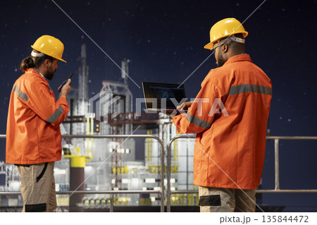 Offshore sea platform engineers use artificial intelligence software on laptop to optimize drilling operations at night. Crew workers monitor barge activity using automated AI systems Offshore sea platform engineers use artificial intelligence software on laptop to optimize drilling operations at night. Crew workers monitor barge activity using automated AI systems 135844472
