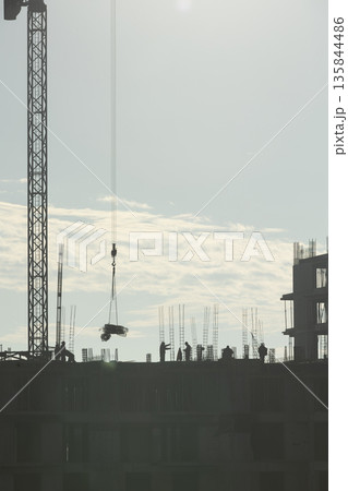 Construction company personnel building high rise condominium for new residential district project during sunny day. Ironworkers constructing concrete skyscraper structures during city expansion Construction company personnel building high rise condominium for new residential district project during sunny day. Ironworkers constructing concrete skyscraper structures during city expansion 135844486