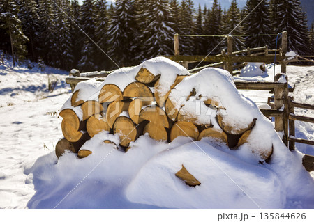 Neatly piled stack of chopped dry trunks wood covered with snow outdoors on bright cold winter sunny day, abstract background, Fire wood logs prepared for winter, ready for burning. Neatly piled stack of chopped dry trunks wood covered with snow outdoors on bright cold winter sunny day, abstract background, Fire wood logs prepared for winter, ready for burning. 135844626