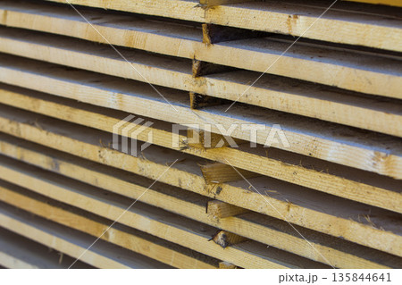 Close-up of neatly piled stack of natural brown rough wooden boards. Industrial timber for carpentry, building, repairing and furniture. Close-up of neatly piled stack of natural brown rough wooden boards. Industrial timber for carpentry, building, repairing and furniture. 135844641