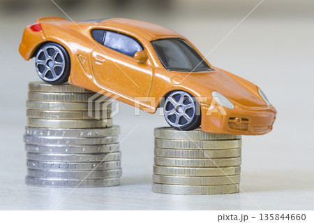 Close-up photo of new bright shiny yellow luxurious expensive toy sport car on two piles of metallic golden and silver coins as symbol of financial prosperity, wealth, vehicle sale and purchase. Close-up photo of new bright shiny yellow luxurious expensive toy sport car on two piles of metallic golden and silver coins as symbol of financial prosperity, wealth, vehicle sale and purchase. 135844660