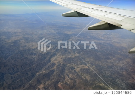 View through airplane window of commercial jet plane wing flying high in the sky. Air travelling concept View through airplane window of commercial jet plane wing flying high in the sky. Air travelling concept 135844686