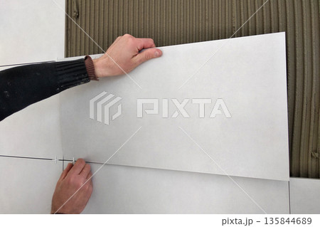 Worker hands putting ceramic tiles on the wall. 135844689