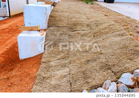 Workers lay down grass on ground next to driveway to create new lawn area for landscaping. 135844895