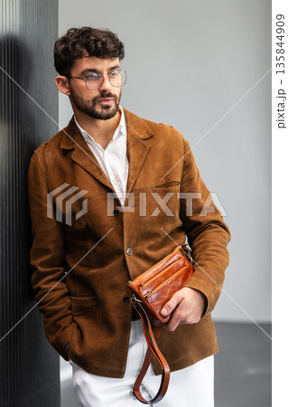 Close up of a stylish man in a brown suede jacket holding a tan leather wristlet clutch bag Close up of a stylish man in a brown suede jacket holding a tan leather wristlet clutch bag 135844909