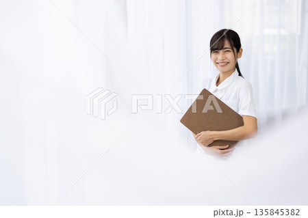 バインダーを抱えて微笑む白衣を着た若い女性 135845382