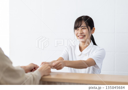 受付でカードを受け取る白衣姿の女性 135845684
