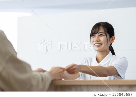 受付でカードを受け取る白衣姿の女性 135845687