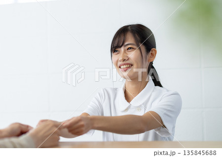 受付でカードを受け取る白衣姿の女性 受付でカードを受け取る白衣姿の女性 135845688