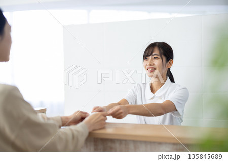 受付でカードを受け取る白衣姿の女性 135845689