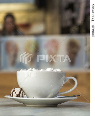 Mug of coffee with marshmallows on porcelain plate on blurred colorful interior bokeh background. 135846505