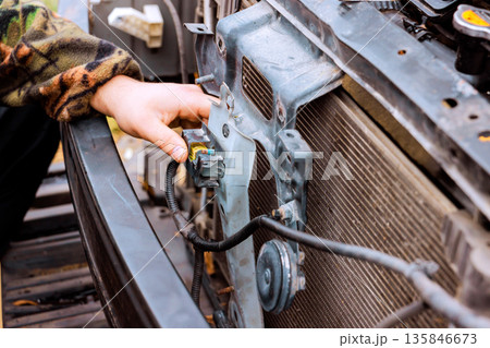 Worker works on front of vehicle, checking fixing parts near radiator Worker works on front of vehicle, checking fixing parts near radiator 135846673