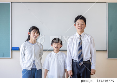 黒板の前に立つ3人の小中学生 135846775