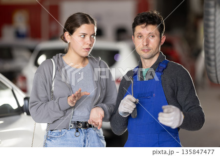 Man car mechanic talks with girl client in workshop and takes order. Man car mechanic talks with girl client in workshop and takes order. 135847477