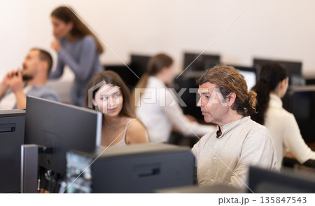 Adult man working on computer talking to woman Adult man working on computer talking to woman 135847543