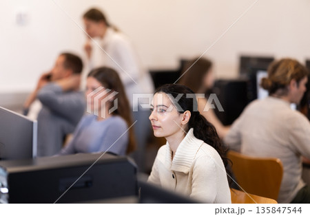 Girl student of computer courses looks at monitor screen, types on keyboard and does work Girl student of computer courses looks at monitor screen, types on keyboard and does work 135847544