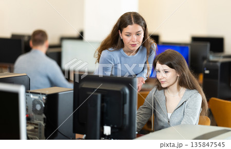 Young female teacher helps woman work on computer Young female teacher helps woman work on computer 135847545
