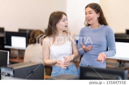 Two female students are chatting cheerfully in university computer lab Two female students are chatting cheerfully in university computer lab 135847558