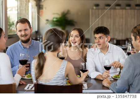 Group of positive friends, men and women, are sitting at a table in a restaurant. They are chatting and drinking wine Group of positive friends, men and women, are sitting at a table in a restaurant. They are chatting and drinking wine 135847738
