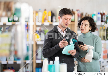Female salesperson offers to buy a spray glass cleaner while a man checks a QR code using smartphone Female salesperson offers to buy a spray glass cleaner while a man checks a QR code using smartphone 135847801