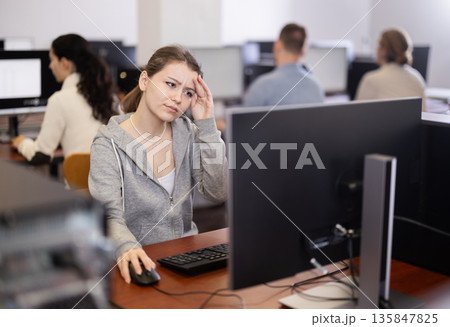 Young woman student of computer courses looks at monitor screen, types on keyboard and does work Young woman student of computer courses looks at monitor screen, types on keyboard and does work 135847825