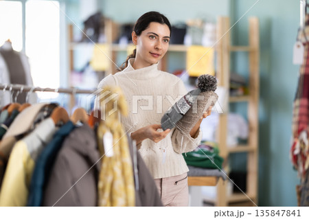 Stylish happy young girl choose hat for autumn-winter season in clothing store. Sale of winter clothing collection Stylish happy young girl choose hat for autumn-winter season in clothing store. Sale of winter clothing collection 135847841