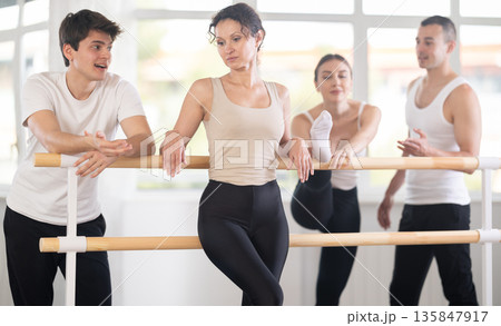 Group of cheerful relaxed women and men casually socializing and stretching beside ballet barre after dance practice in choreography studio 135847917