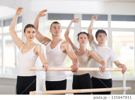 Female ballet teacher exhibiting third position at barre during group class Female ballet teacher exhibiting third position at barre during group class 135847931