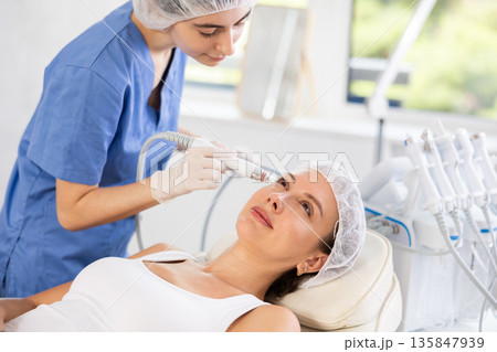 Young woman cosmetologist doing cleansing procedure to young woman 135847939