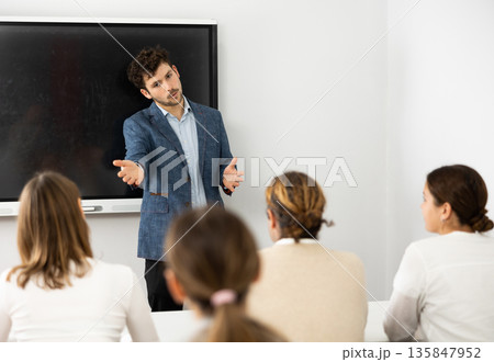 Young male tutor teaching students in college classroom Young male tutor teaching students in college classroom 135847952