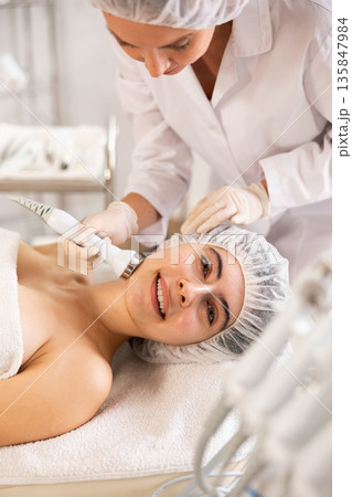 Female client undergoing anti-aging ultrasonic phonophoresis procedure on face 135847984