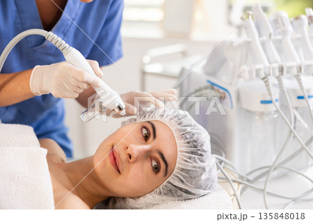 Young woman cosmetologist doing moisturizing procedure to young woman 135848018