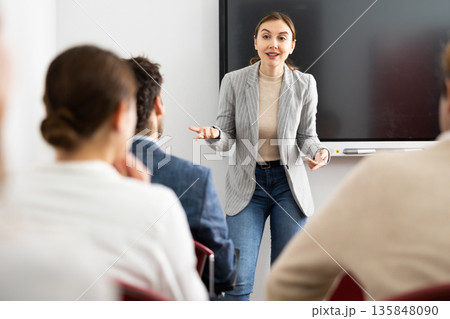 Young woman standing near interactive board and communicating with adult students during advanced training courses in classroom Young woman standing near interactive board and communicating with adult students during advanced training courses in classroom 135848090