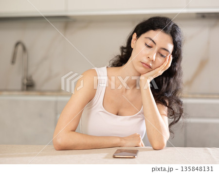 Young upset woman waiting for call sitting at table Young upset woman waiting for call sitting at table 135848131
