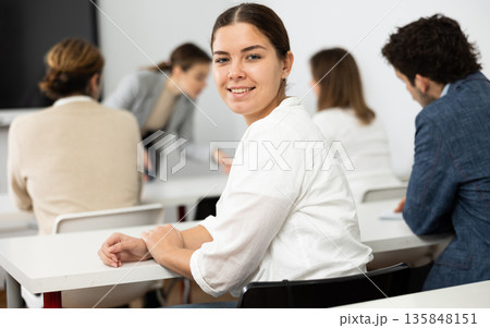 Portrait of smiling young woman smiling at camera during studying of foreign language with group of students in class Portrait of smiling young woman smiling at camera during studying of foreign language with group of students in class 135848151