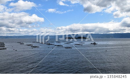 日本の穏やかな内海の湾内に浮かぶ多数の養殖筏と遠くに見える山並みが織りなすのどかな漁村の風景 日本の穏やかな内海の湾内に浮かぶ多数の養殖筏と遠くに見える山並みが織りなすのどかな漁村の風景 135848245
