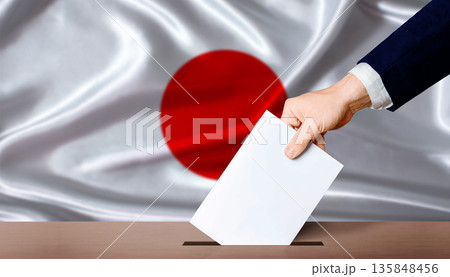 Hand placing a ballot in ballot box with the Japanese flag in the background. Japan presidential vote 2026 135848456